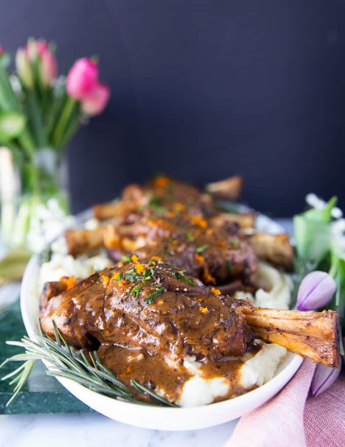 side view of the lamb shanks on a plate surrounded by fresh rosemary 
