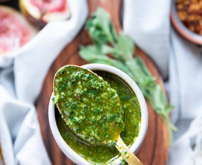A spoon showing the dripping chermoula sauce over a bowl