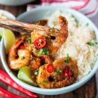 A chop stick holding a chilli lime shrimp cooked over white rice