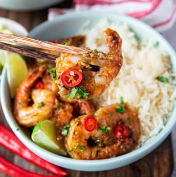 A chop stick holding a chilli lime shrimp cooked over white rice