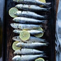Flavored sardines on a baking sheet with lemon slices ready to go in the oven to bake