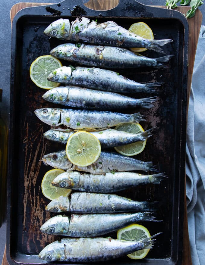 Flavored sardines on a baking sheet with lemon slices ready to go in the oven to bake