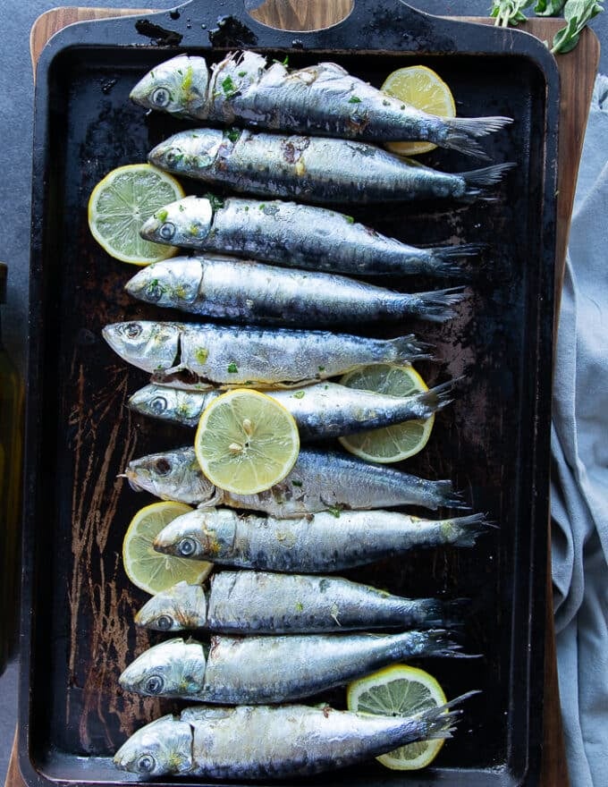 Flavored sardines on a baking sheet with lemon slices ready to go in the oven to bake
