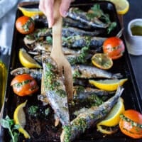 A hand holding a cooked sardine with a wooden spoon showing the perfectly cooked fish