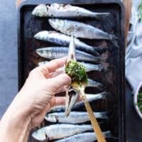 A spoon slathering the ingredients for sardine recipe inside the gut of fresh sardines to flavor it