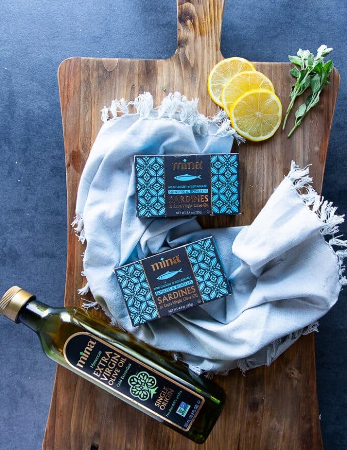 two boxes of canned sardines on a board surrounded by lemon slices