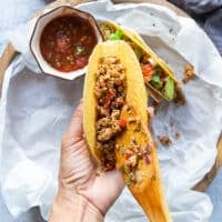 A hand loading the ready tacos with the ground chicken mixture filling up the taco shell