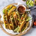 A large plate of ground chicken tacos loaded with avocados, tomatoes, onions, alongside a bowl of homemade salsa and lime wedges