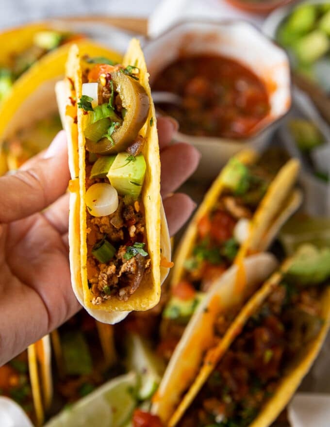 A hand holding a finished and loaded ground chicken taco with avocado, jalapenos, scallions and more