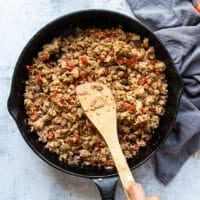 Ground chicken mixture cooking in a cast iron skillet with onions, bell peppers and spice