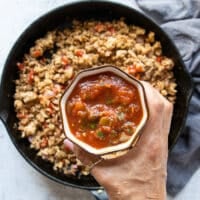 A hand holding homemade salsa to be added into the ground chicken mixture