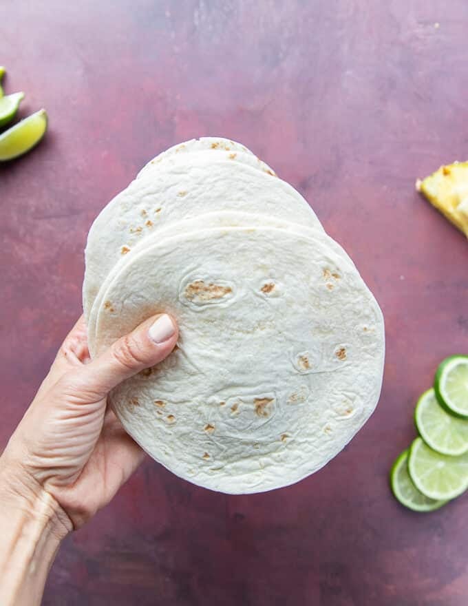 A hand holding flour tortillas to make lamb taco