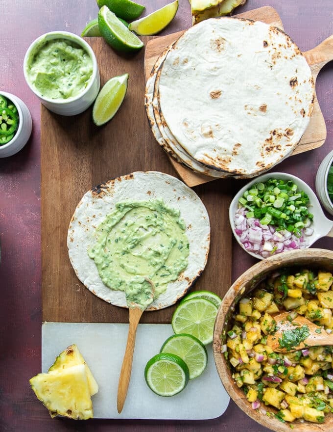 A hand spreading a layer of avocado crema on the tortilla