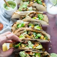 A hand placing the assembled lamb tacos on a taco holder