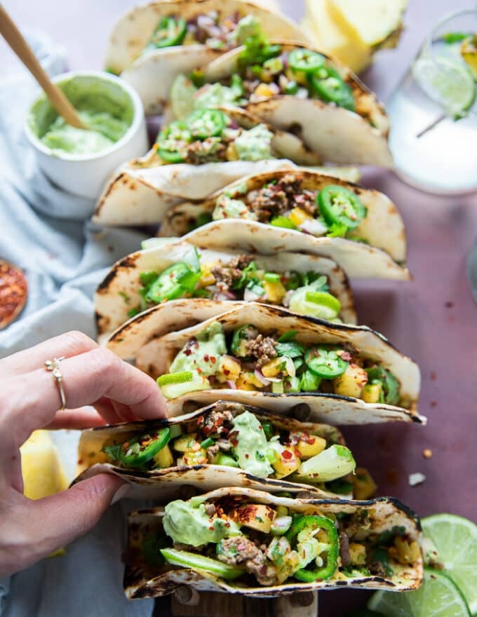 Eine Hand, die die zusammengesetzten Lamm-Tacos auf einen Taco-Halter legt 