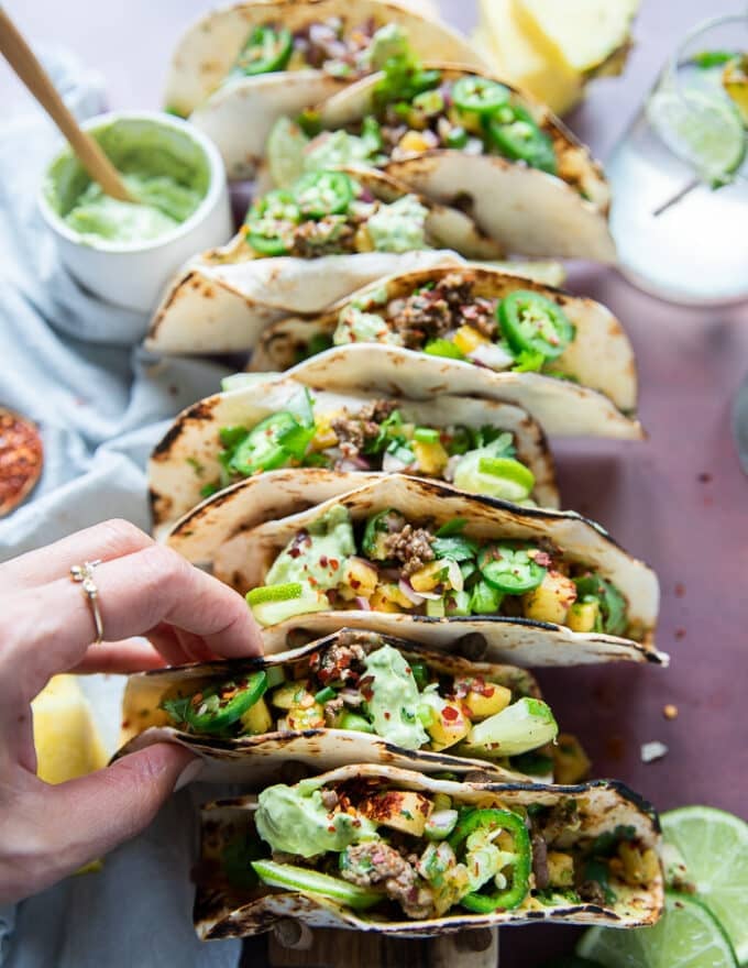 A hand placing the assembled lamb tacos on a taco holder 