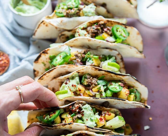 A hand placing the assembled lamb tacos on a taco holder