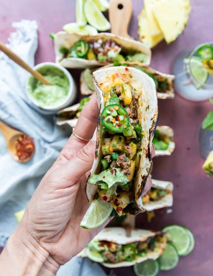 A hand holding a lamb taco showing up close the filling and toppings