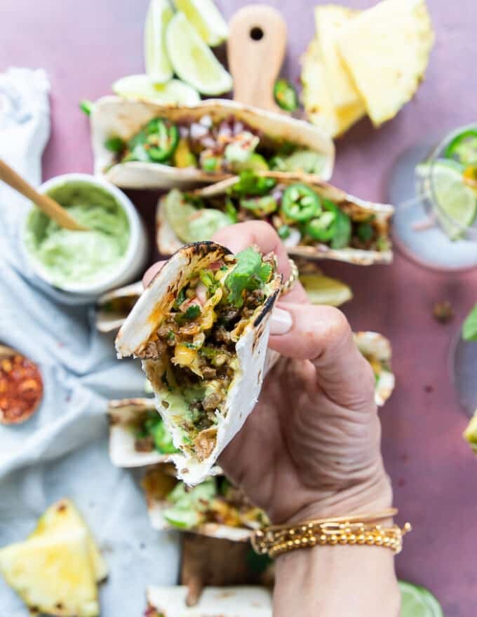 A hand holding a bitten lamb tacos showing the inside filling and toppings of the tacos