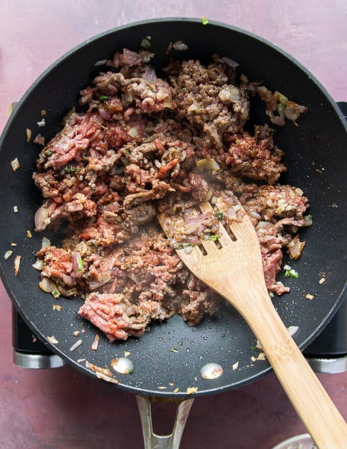 The lamb with spices, garlic going into the onion mixture and a wooden spoon mixing in the meat