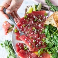 A fork taking a piece of tuna carpaccio off the plate to show the final dish