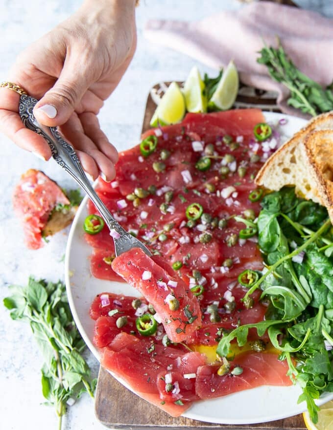 A fork taking a piece of tuna carpaccio off the plate to show the final dish