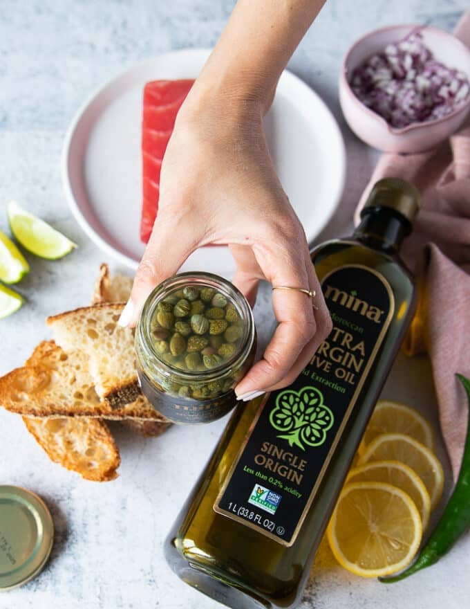 A hand holding a jar of capers showing the type of capers used for carpaccio tuna recipe