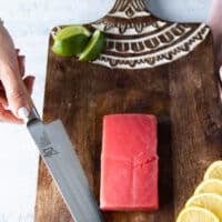 A hand holding a super sharp knife ready to slice the tuna