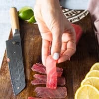 A hand holding a super thin slice of sliced tuna to show how thin it should be to make carpaccio