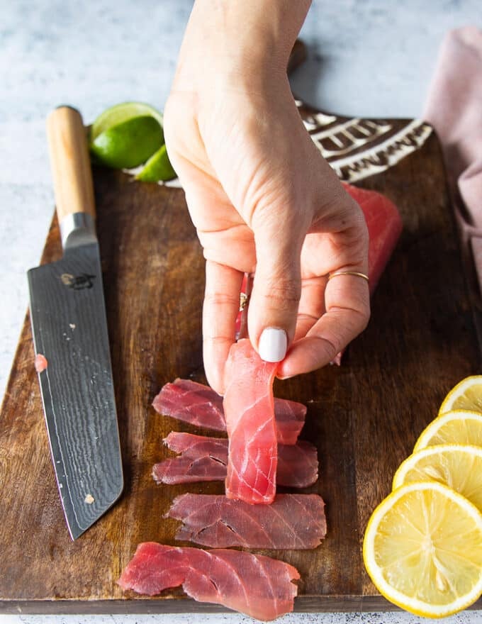 A hand holding a super thin slice of sliced tuna to show how thin it should be to make carpaccio