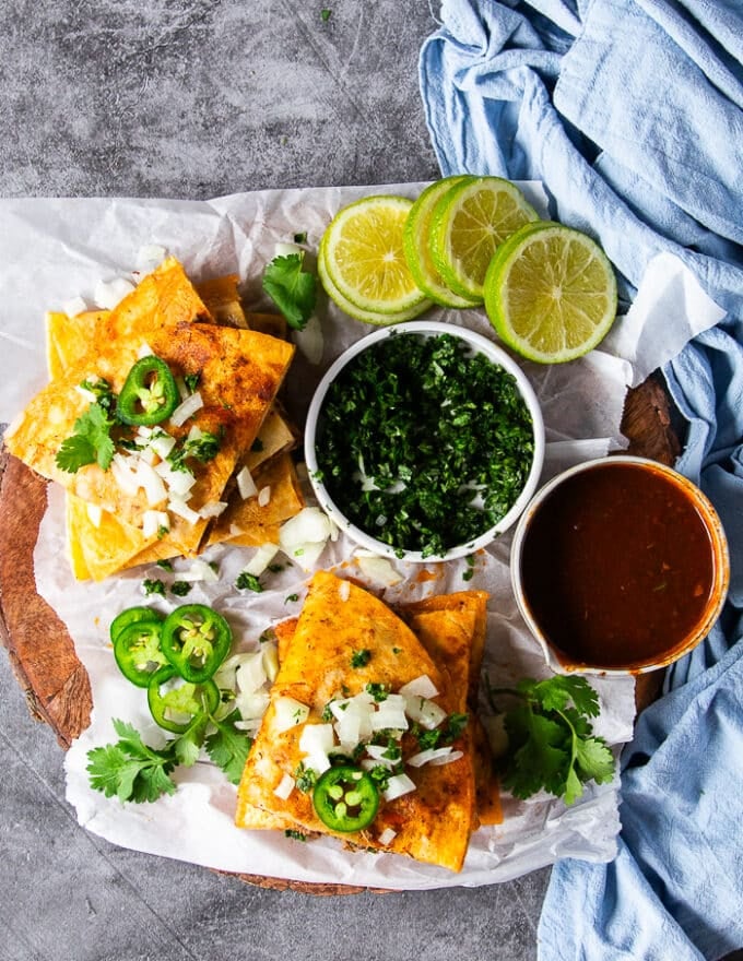 Top view of Birria quesadillas cut up and surrounded with a bowl of birria sauce for dipping, some cilantro and chopped onions and jalapeno extra 