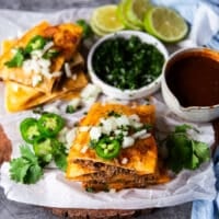 Cut up birria quessadillas golden right off the pan and topped with cilantro, chopped onions and jalapenos with a side bowl of birria stew for dipping