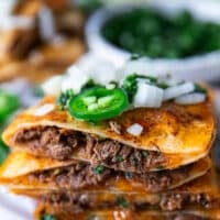 Close up of a cut open birria quesadilla showing the birria meat and cheese and onion jalapeño topping