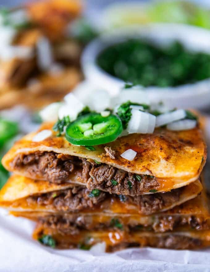 Close up of a cut open birria quesadilla showing the birria meat and cheese and onion jalapeño topping 