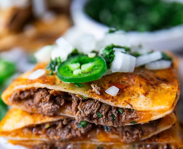 Close up of a cut open birria quesadilla showing the birria meat and cheese and onion jalapeño topping