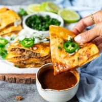 A hand dipping the birria quesadilla right into the bowl of birria stew