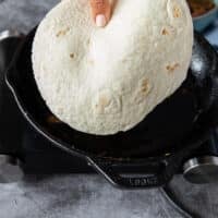 A hand holding a tortilla ready to put in a hot pan over medium heat with some oil