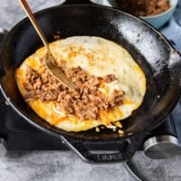 A fork adding a generous amount of birria meat over the cheese on the tortilla