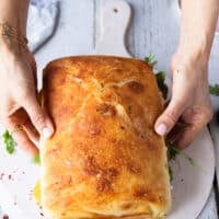 A hand puttin the top of the bread over to close the caprese sandwich and press it down slightly before slicing it