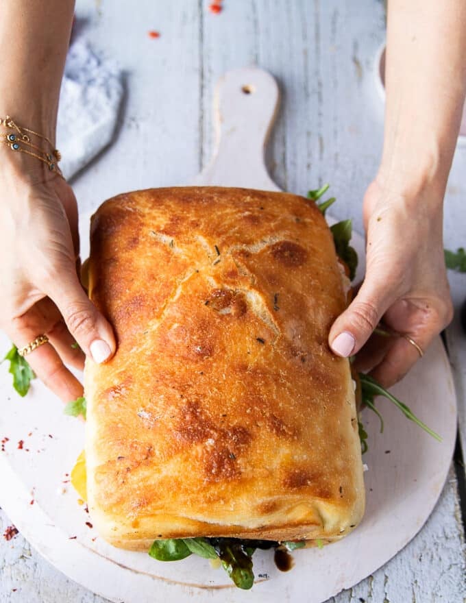 A hand puttin the top of the bread over to close the caprese sandwich and press it down slightly before slicing it 