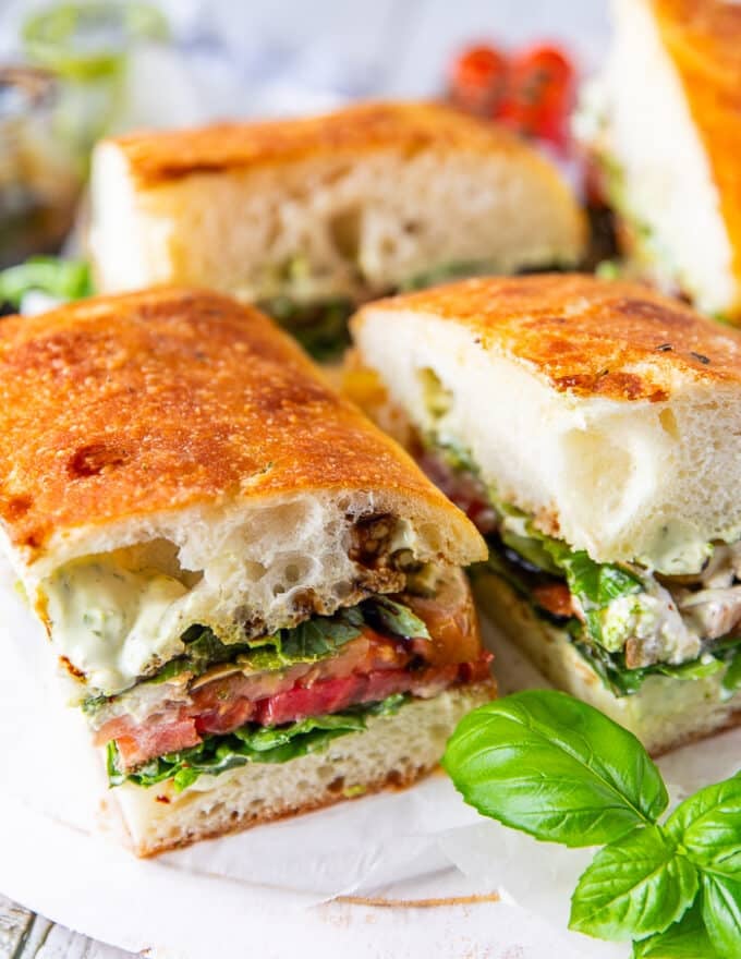 Cut up caprese sandwiches on a board surrounded by fresh basil leaves and fresh tomatoes