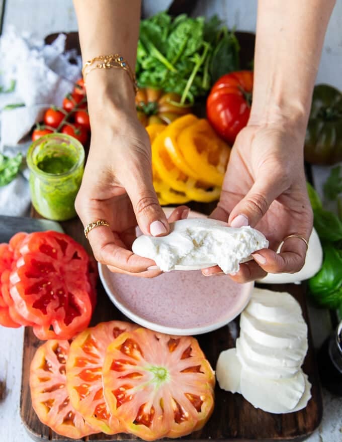 A hand holding a piece of burrata cheese cutting it apart showing the inside texture