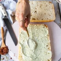 A hand spreading a layer of basil mayo over the bread to start making caprese sandwich