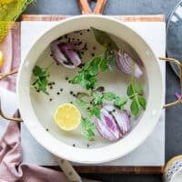 A pot filled with water, onion halves, lemon slices, fresh herbs, bay leaves, whole peppercorn and seasoning on the stove ready to boil for the octopus