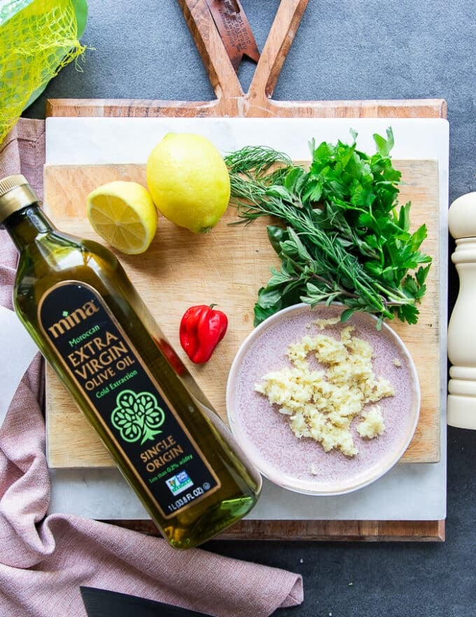 Ingredients to make grilled octopus including olive oil, garlic, chillies, fresh herbs, lemon juice, seasoning
