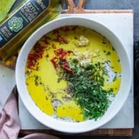 All the marinade ingredients added on to a shallow plate including olive oil, lemon juice, garlic, fresh herbs, seasoning