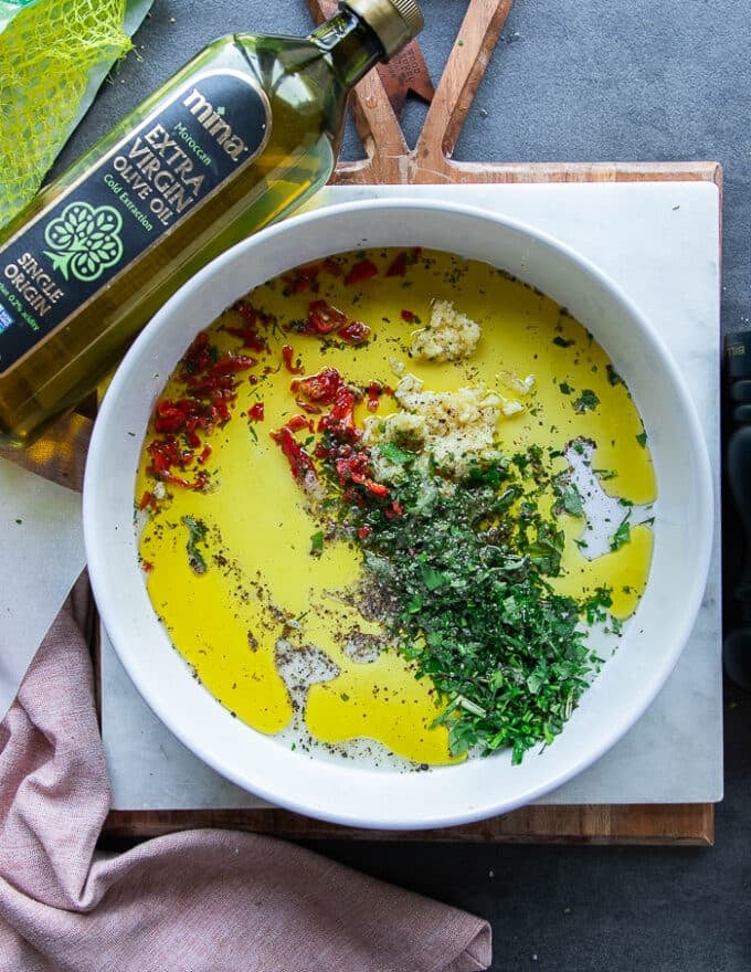 All the marinade ingredients added on to a shallow plate including olive oil, lemon juice, garlic, fresh herbs, seasoning 