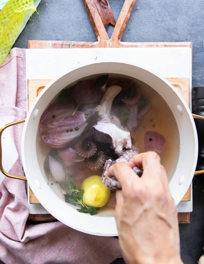 A hand dropping in the octopus into the pot of flavored boiling water 
