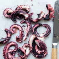 A knife slicing the tentacles of the boiled octopus