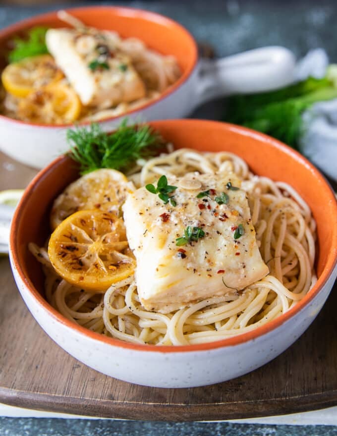 A piece of baked halibut over a bowl of pasta showing one of the ways to cook halibut fish